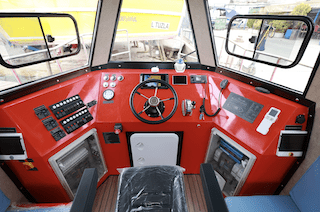 Plast Boat professional HDPE vessel wheelhouse interior featuring a modern control panel, steering wheel, and ergonomic red console design in a shipyard environment.