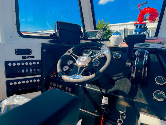 A close-up of the red enclosed helm station on a firefighting boat. The cabin features large panoramic windows for the captain's 360-degree view, with "FIRE RESCUE" printed in white on the side.