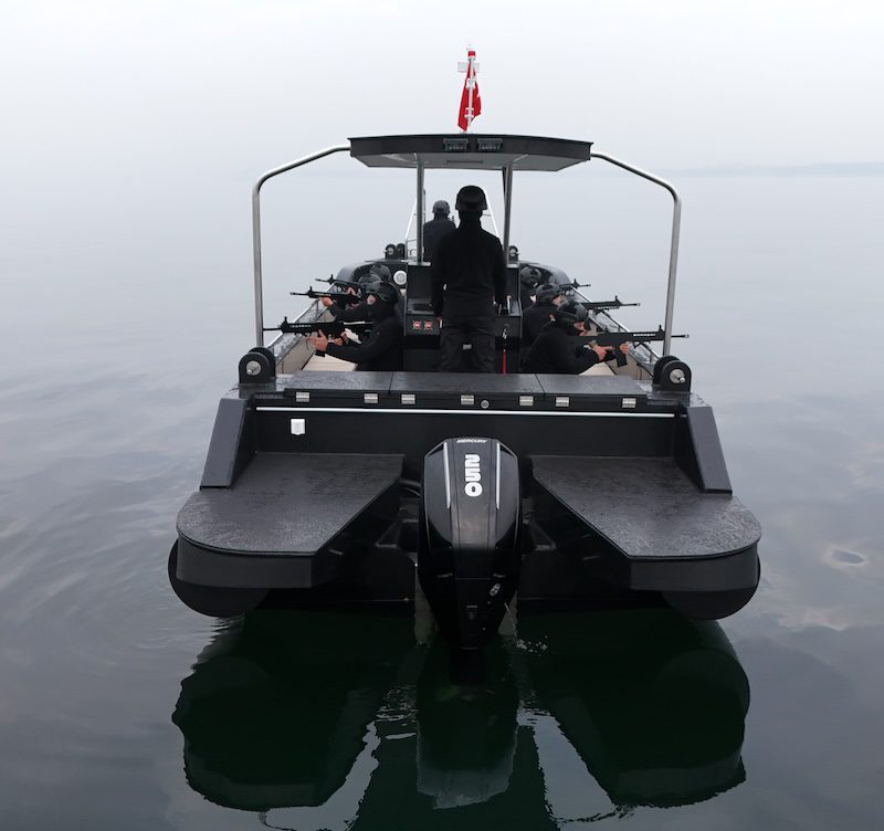 Rear view of a Plast Boat black HDPE patrol boat designed for maritime security and coastal defense. High-speed patrol boat equipped with a 250HP Mercury engine, showing tactical personnel in misty sea conditions.