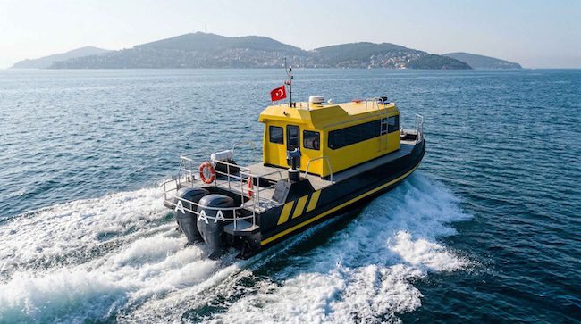 A black and yellow HDPE workboat underway at speed on calm blue waters, displaying a Turkish flag, with forested islands visible in the background.